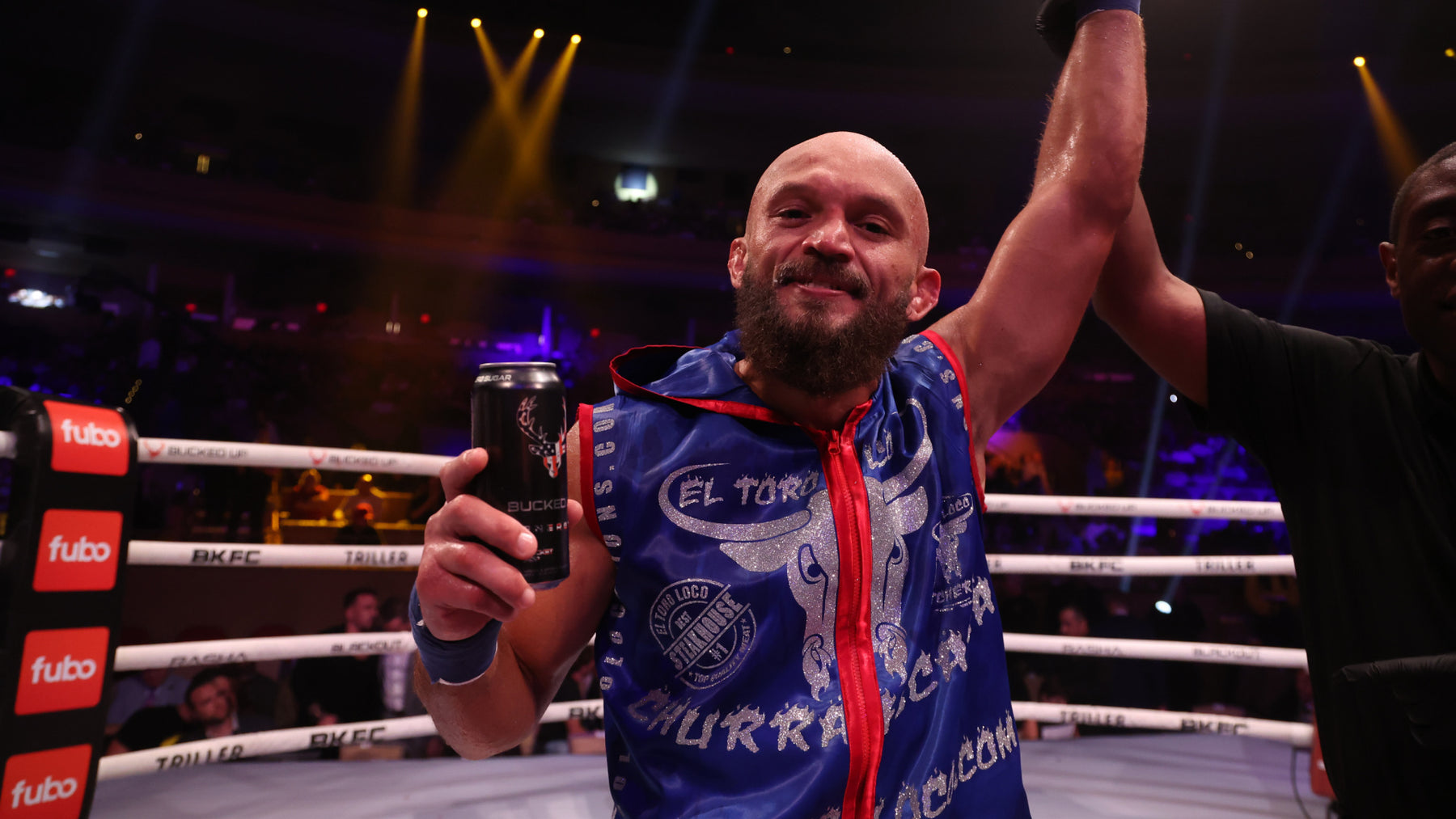 Edgard Plazaola wearing El Toro Loco Merch, celebrating in boxing ring holding 'Bucked Up' drink in one hand, while his other hand is raised.