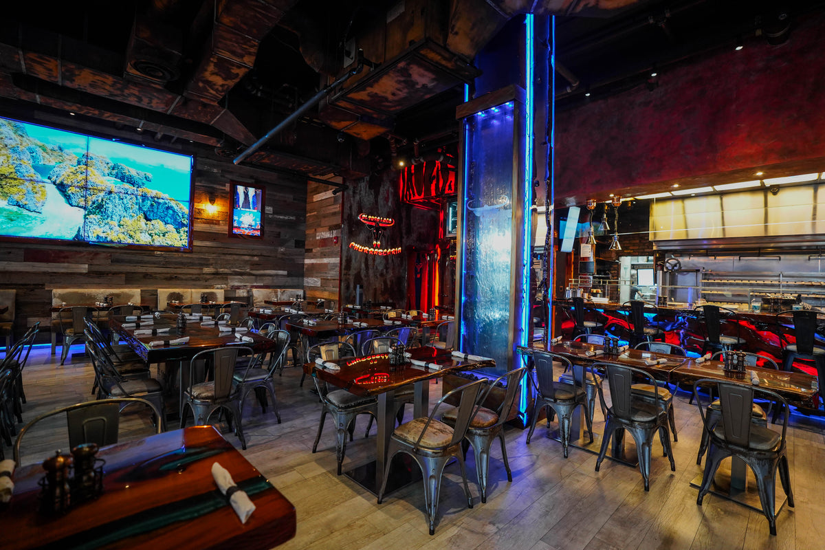 El Toro Loco Steakhouse interior featuring a bar, tables, chairs, and a large screen TV on the wall.