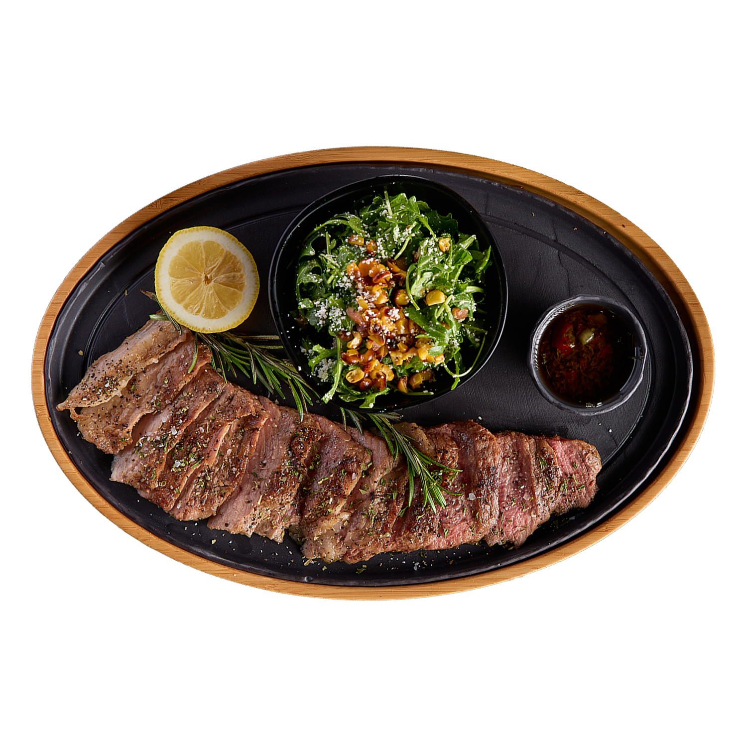 Steak with a side of salad on a black plate with a wooden rim, garnished with lemon and herbs.
