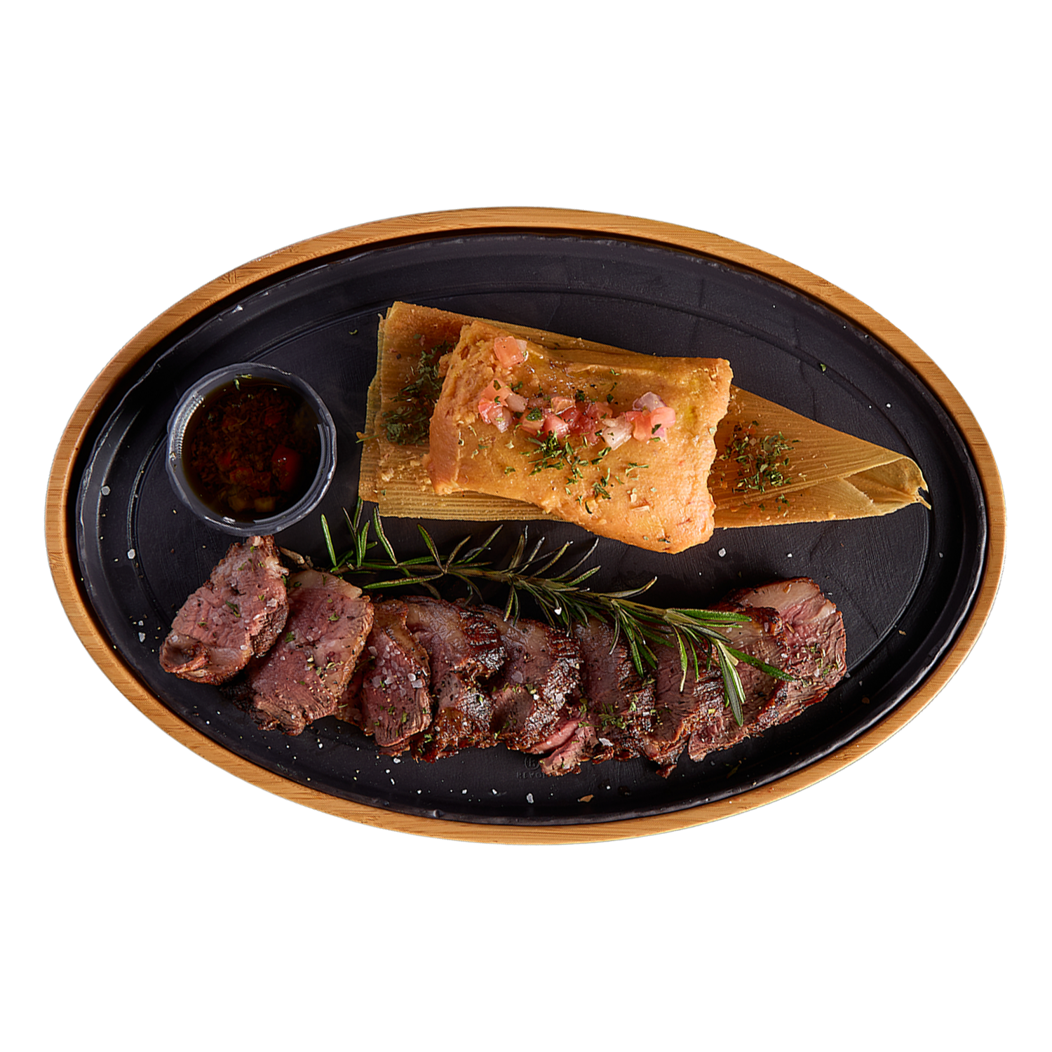Plated dish with sliced meat, tamales, and a small bowl of sauce on a black plate with wooden rim.