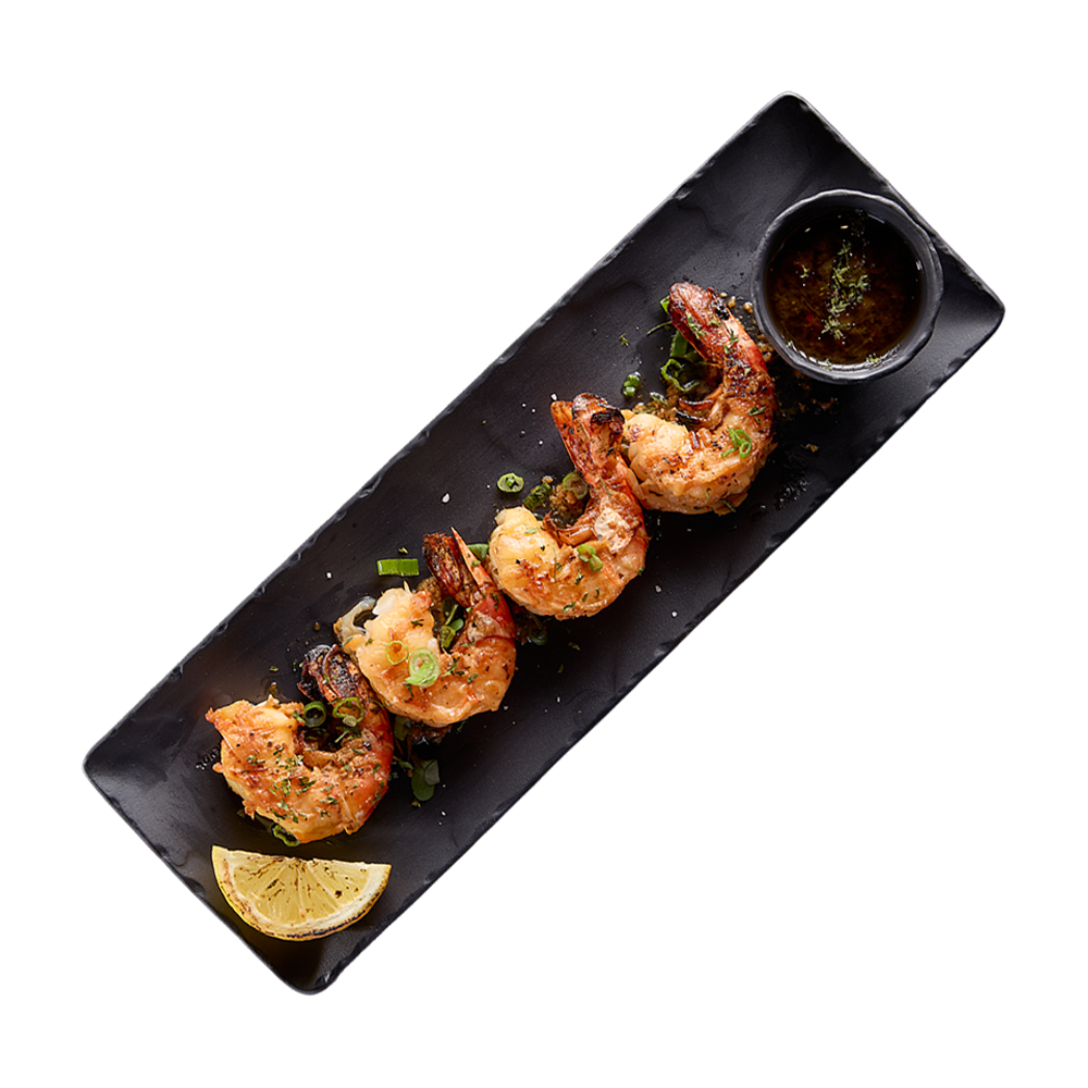 Plated shrimp with a side of sauce and lemon wedge on a black tray